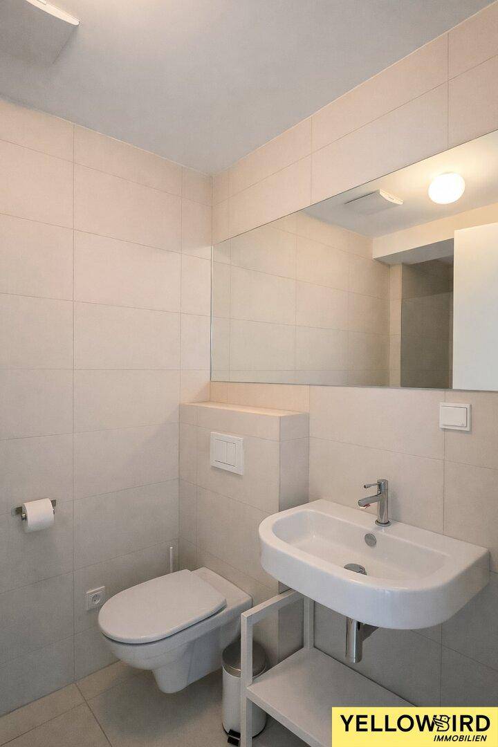 Helles Gäste-WC mit Wand-WC und Waschbecken, ausgestattet mit einem großen Spiegel.