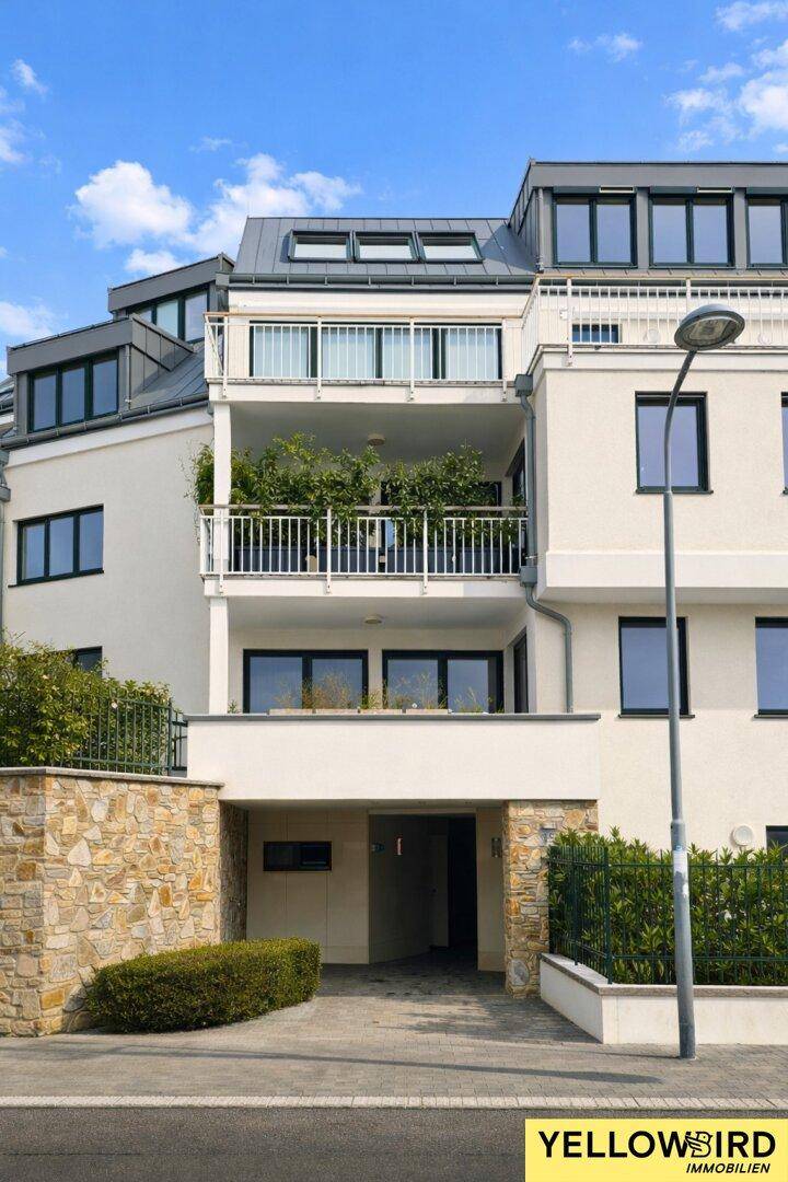 Moderne Gebäudefassade mit Balkonen und Tiefgaragenzufahrt, umgeben von Grünflächen.