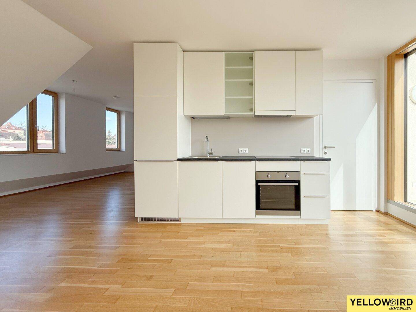 Moderne Einbauküche in Weiß mit dunkler Arbeitsplatte und Holzboden in einem hellen Raum.