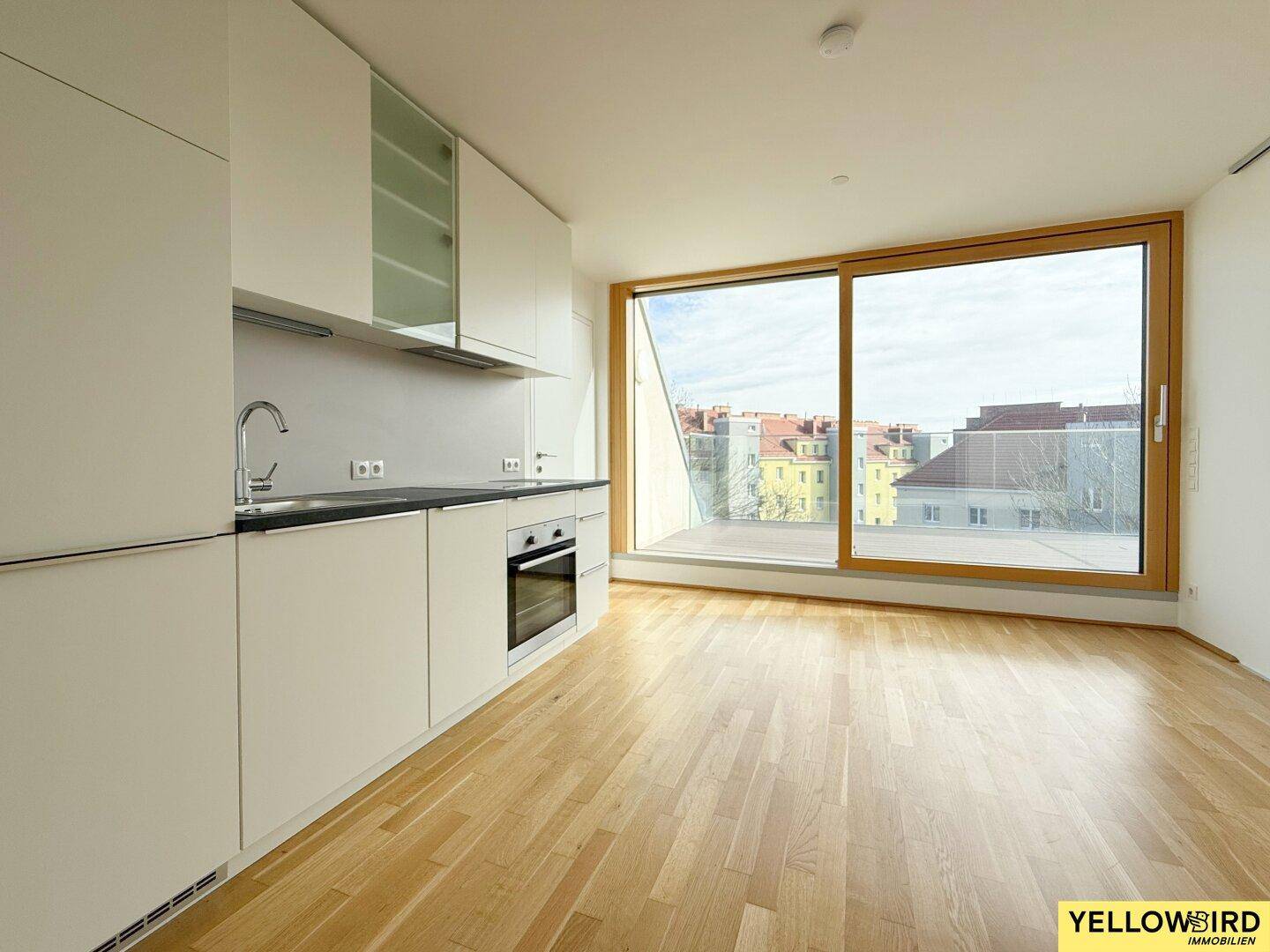 Offener Wohnbereich mit Küchenzeile, Holzboden und großer Schiebetür zur Terrasse.
