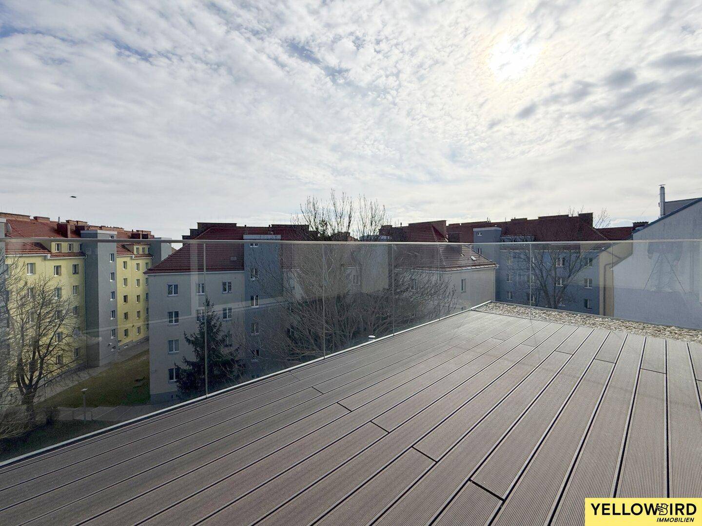 Große Dachterrasse mit Holzdielen und Glasbrüstung, bietet einen weiten Blick über die Stadt.