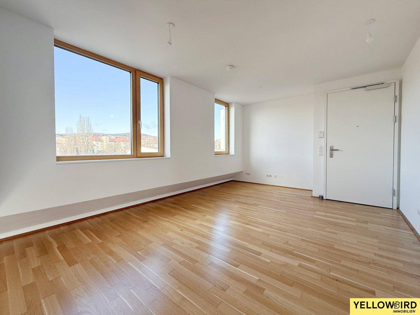 Heller, leerer Wohnraum mit Holzboden und großen Fenstern, bietet viel Tageslicht.