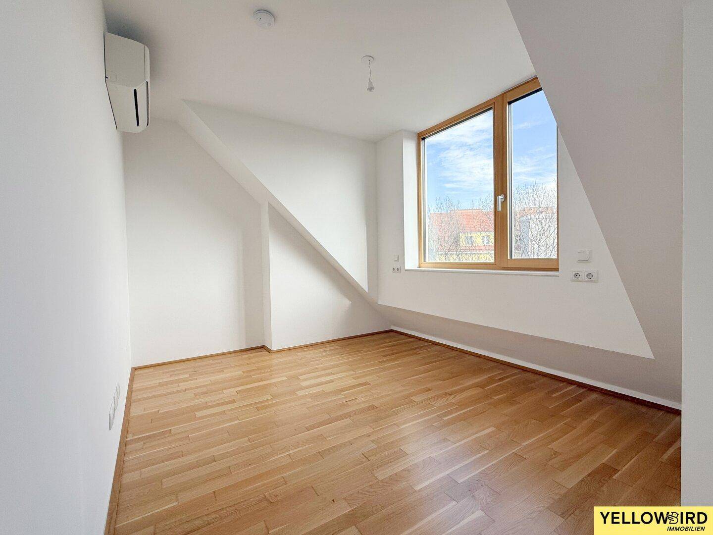 Helles Schlafzimmer mit Holzboden, Dachschräge und Klimaanlage, bietet viel Tageslicht.