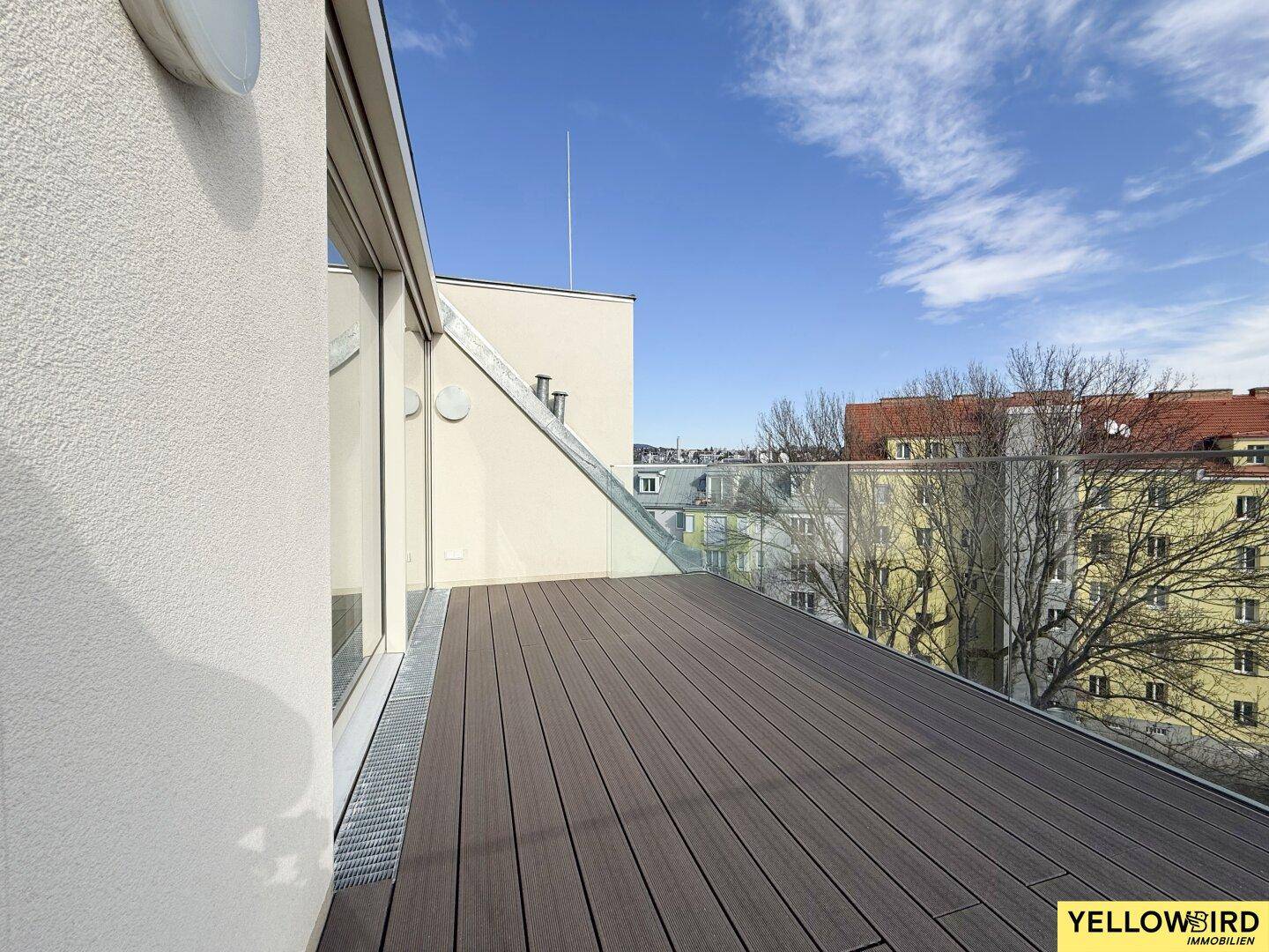 Moderne Dachterrasse mit Holzdielen und Glasgeländer, bietet einen weiten Blick über die Umgebung.