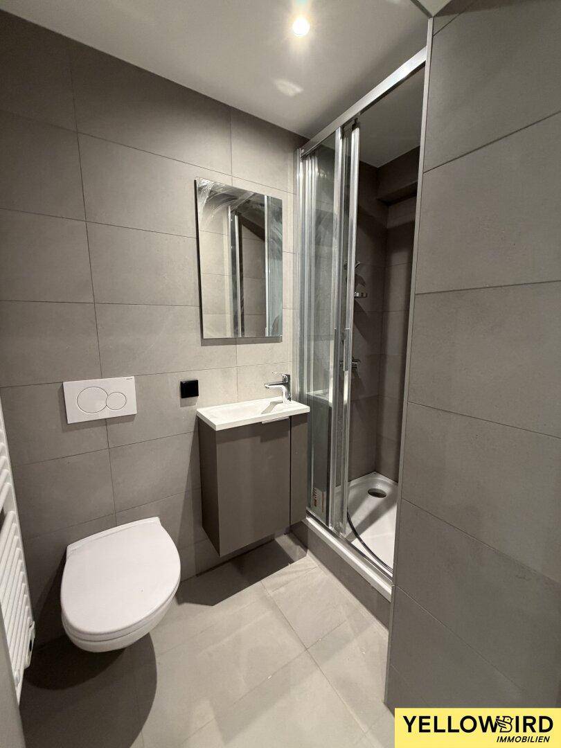 Modernes Badezimmer mit grauen Fliesen, Duschkabine, Waschtisch und wandhängendem WC, sehr gepflegt.