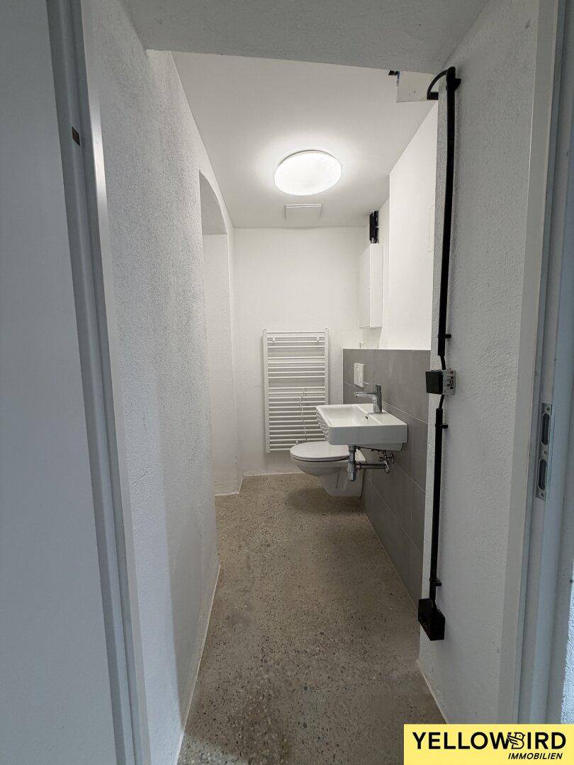 Helles Gäste-WC mit weißen Wänden, grauen Akzentfliesen, Waschtisch und wandhängendem WC.