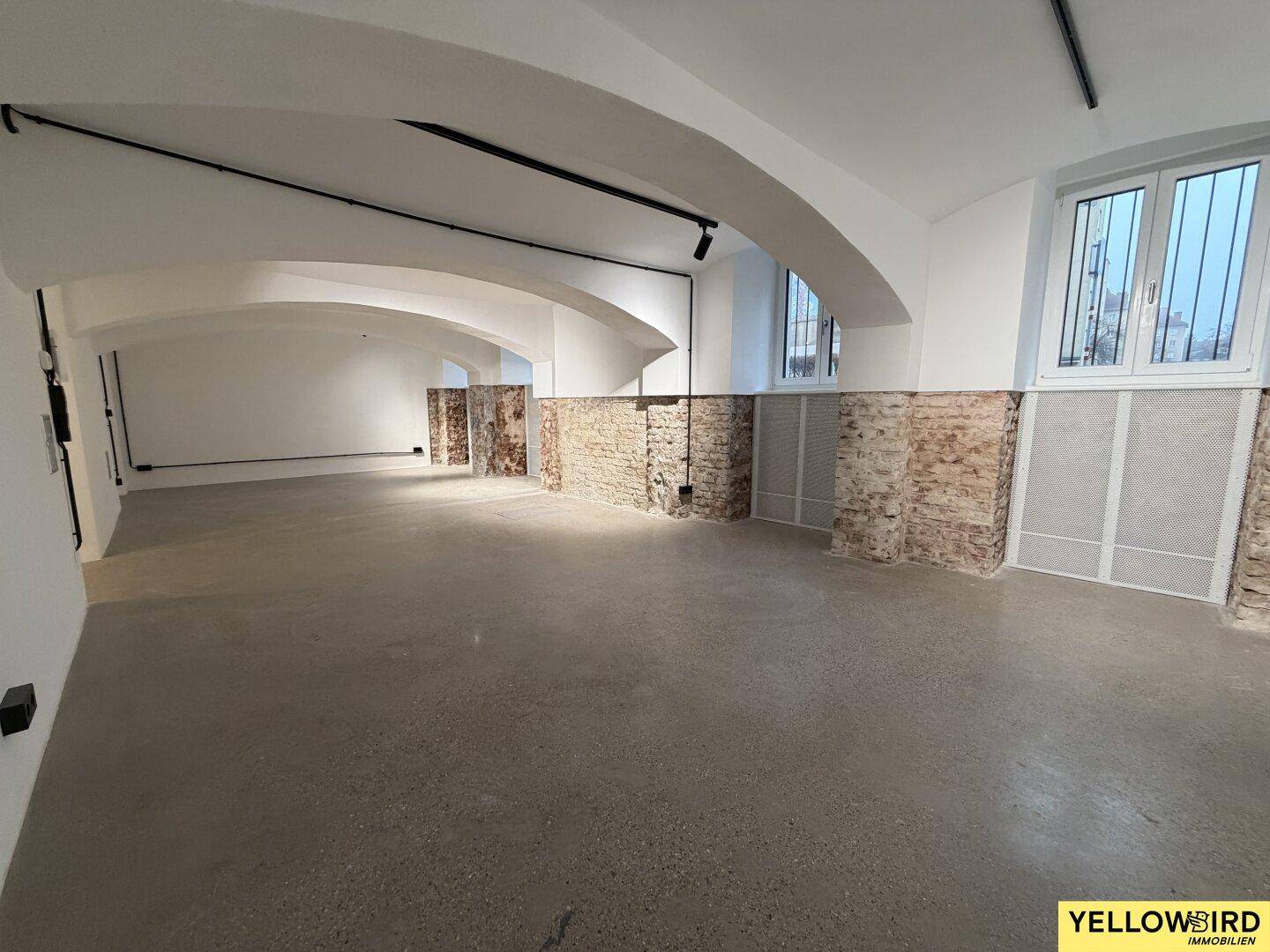 Weitläufiger Gewerberaum mit hohen Gewölbedecken, freigelegten Ziegeldetails und großen Fenstern.