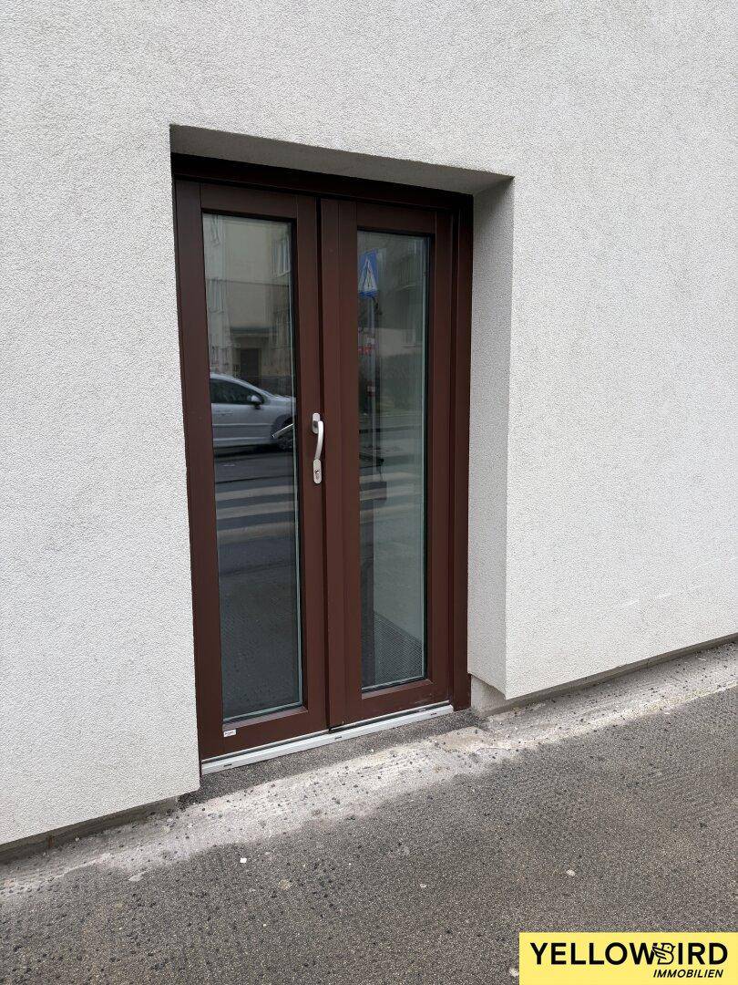 Braune Doppeltür in einer weißen Putzfassade, die direkt zur Straße führt.