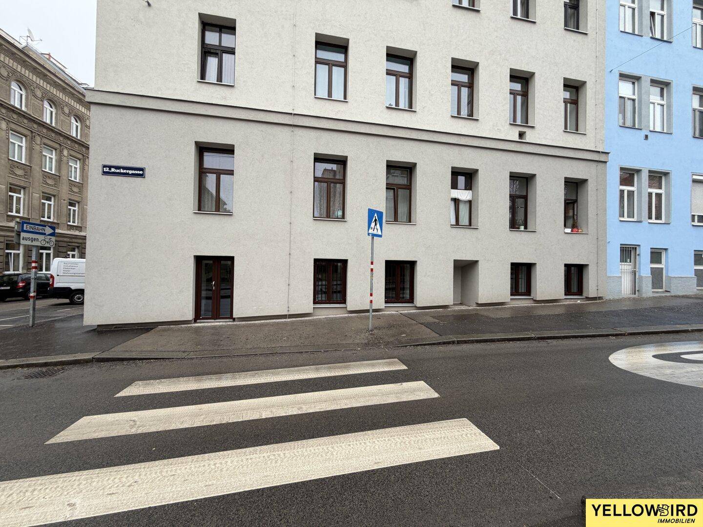 Außenansicht eines Gebäudes mit mehreren Fenstern und Eingängen, von der gegenüberliegenden Straßenseite.