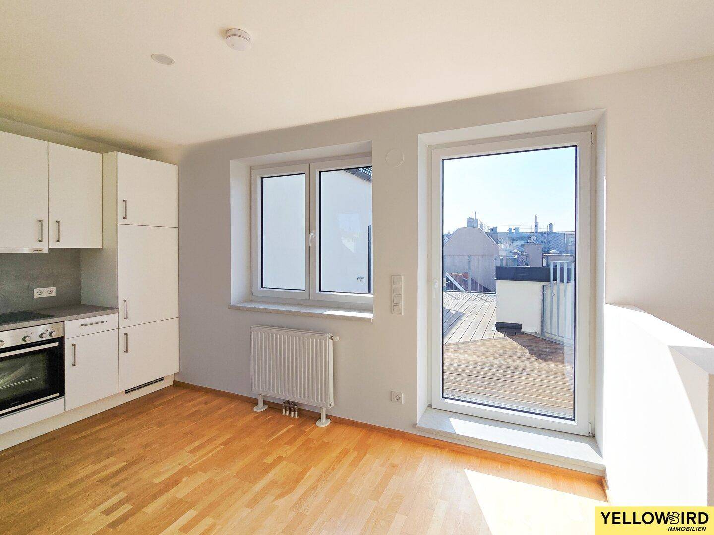 Leere Küche mit weißen Schränken, Holzboden und direktem Zugang zur Terrasse.
