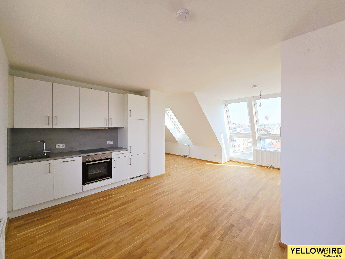 Heller, offener Wohnbereich mit Einbauküche, Holzboden und schrägen Dachfenstern.
