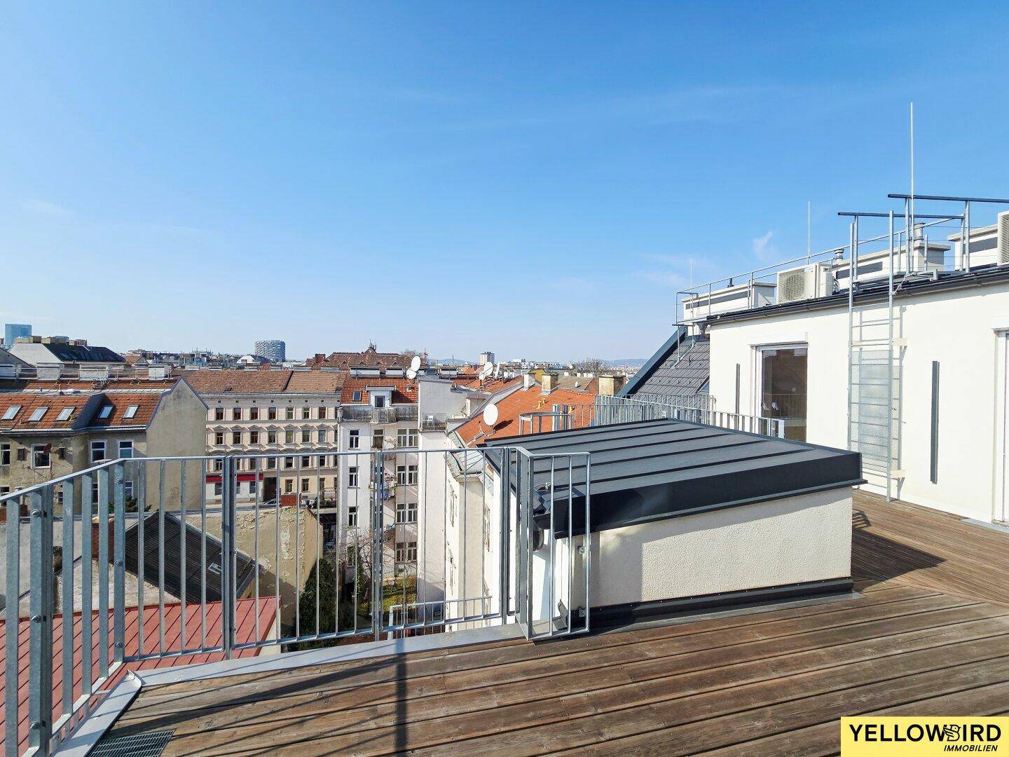 Geräumige Dachterrasse mit Holzboden und weitem Blick über die Dächer der Stadt.