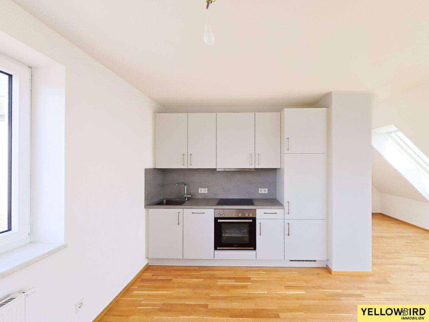 Moderne Einbauküche mit weißen Schränken, grauer Arbeitsplatte und integriertem Backofen.