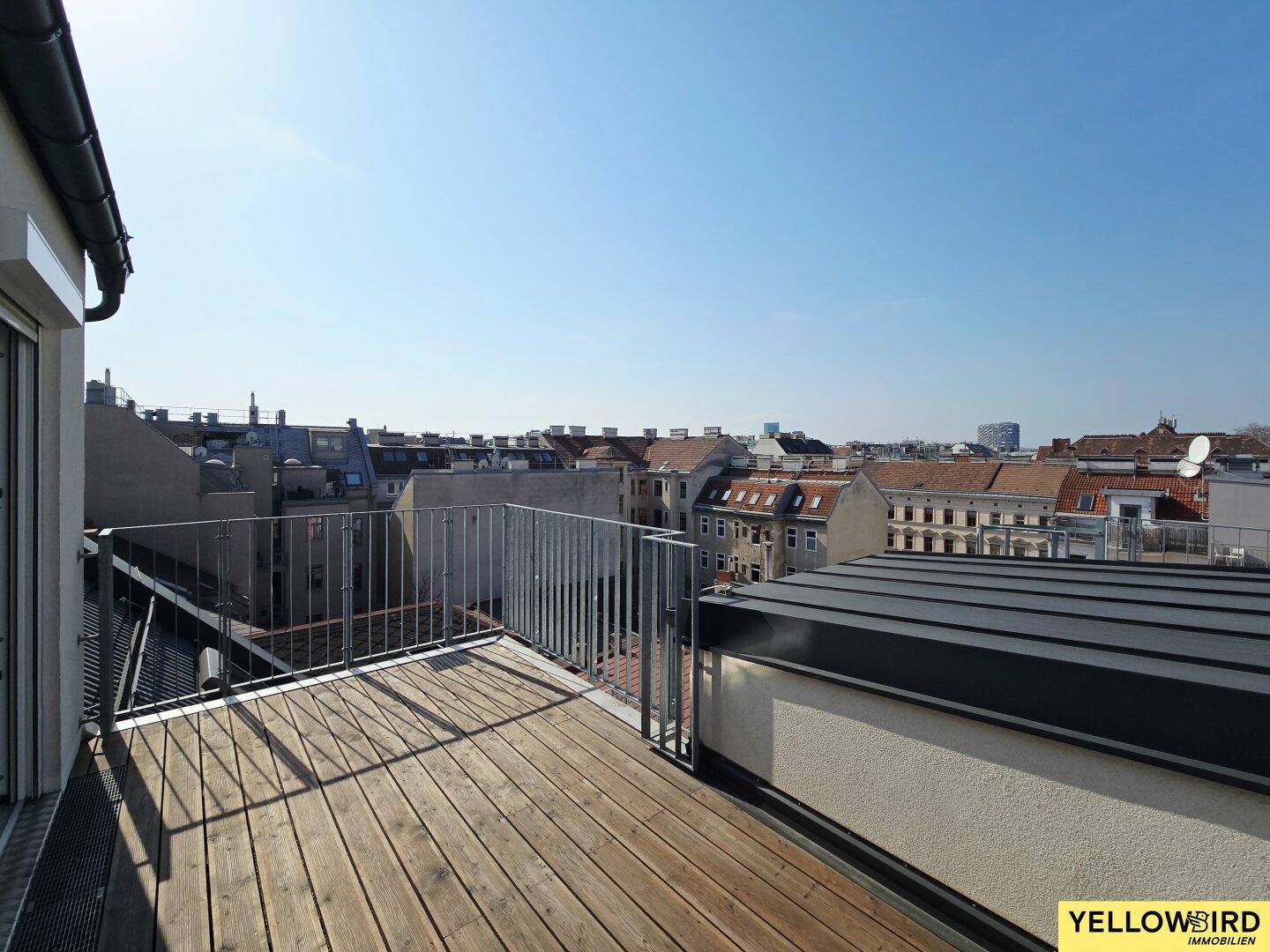 Weitläufige Dachterrasse mit Holzdielen und Panoramablick über die städtische Umgebung.