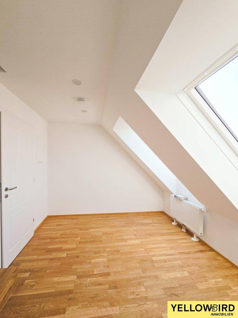 Heller Raum mit Holzboden, weißen Wänden und einem schrägen Dachfenster.