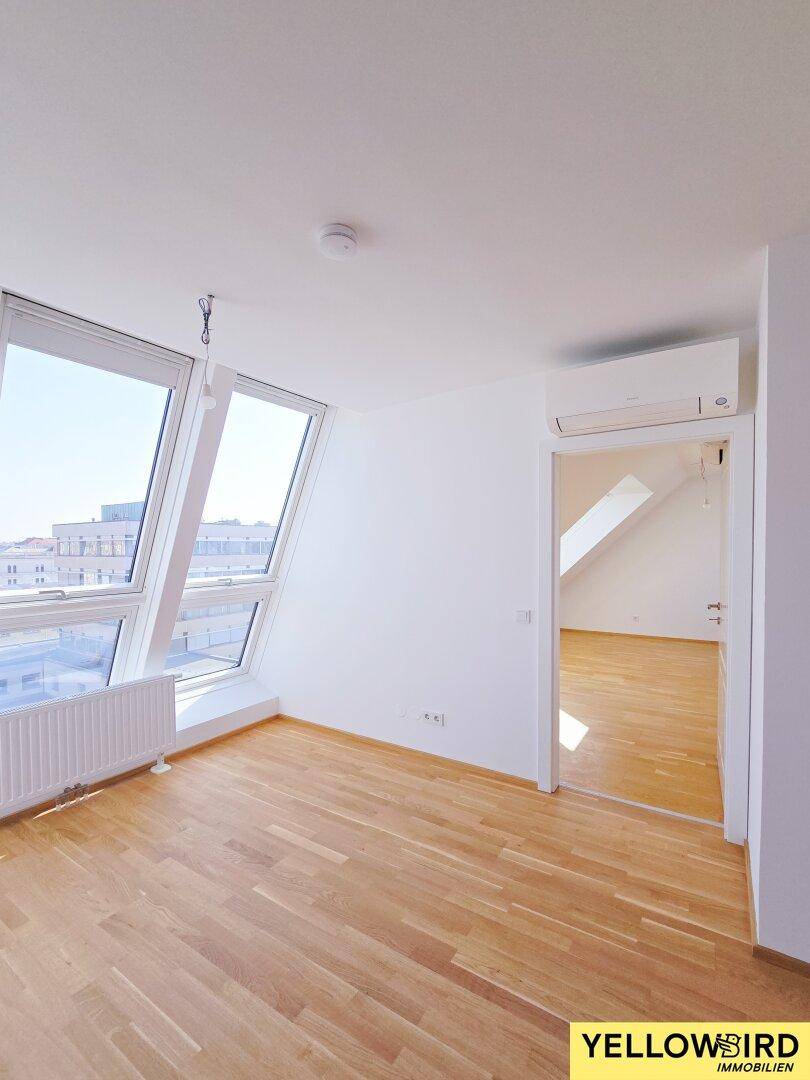 Geräumiger Raum mit Holzboden, großer Fensterfront und Klimaanlage, mit Blick auf die Stadt.