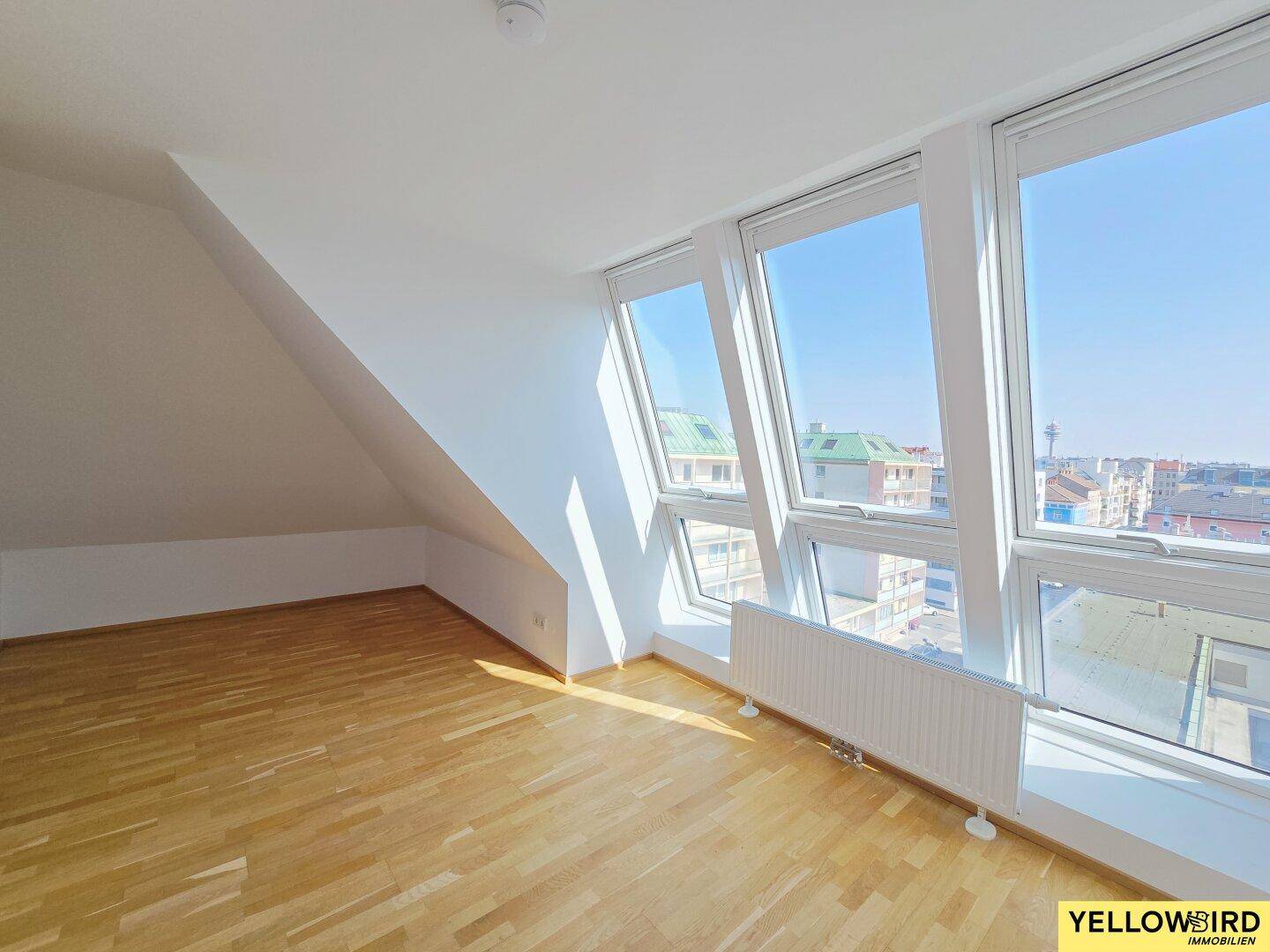Lichtdurchfluteter Raum mit Holzboden und großer Fensterfront, die einen weiten Stadtblick bietet.