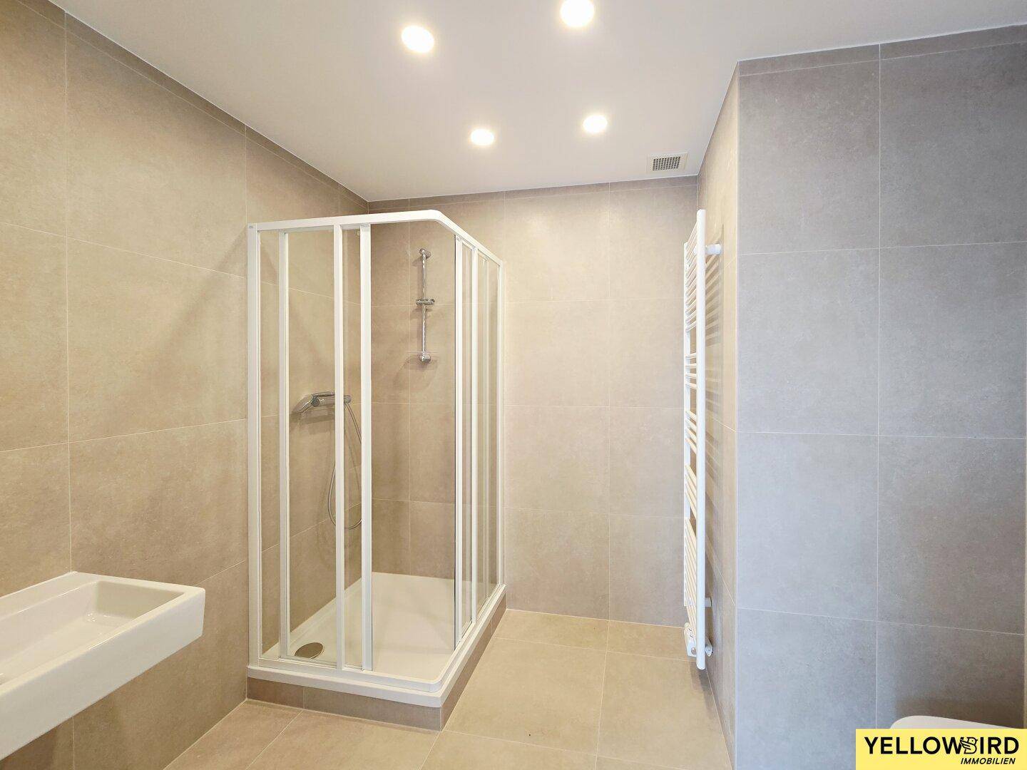 Modernes Badezimmer mit grauen Fliesen, Duschkabine und beheiztem Handtuchhalter.