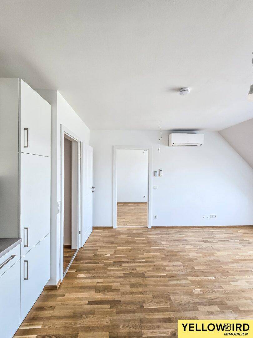 Geräumiger Wohnbereich mit Holzboden, Klimaanlage und Zugang zu weiteren Zimmern im Dachgeschoss.