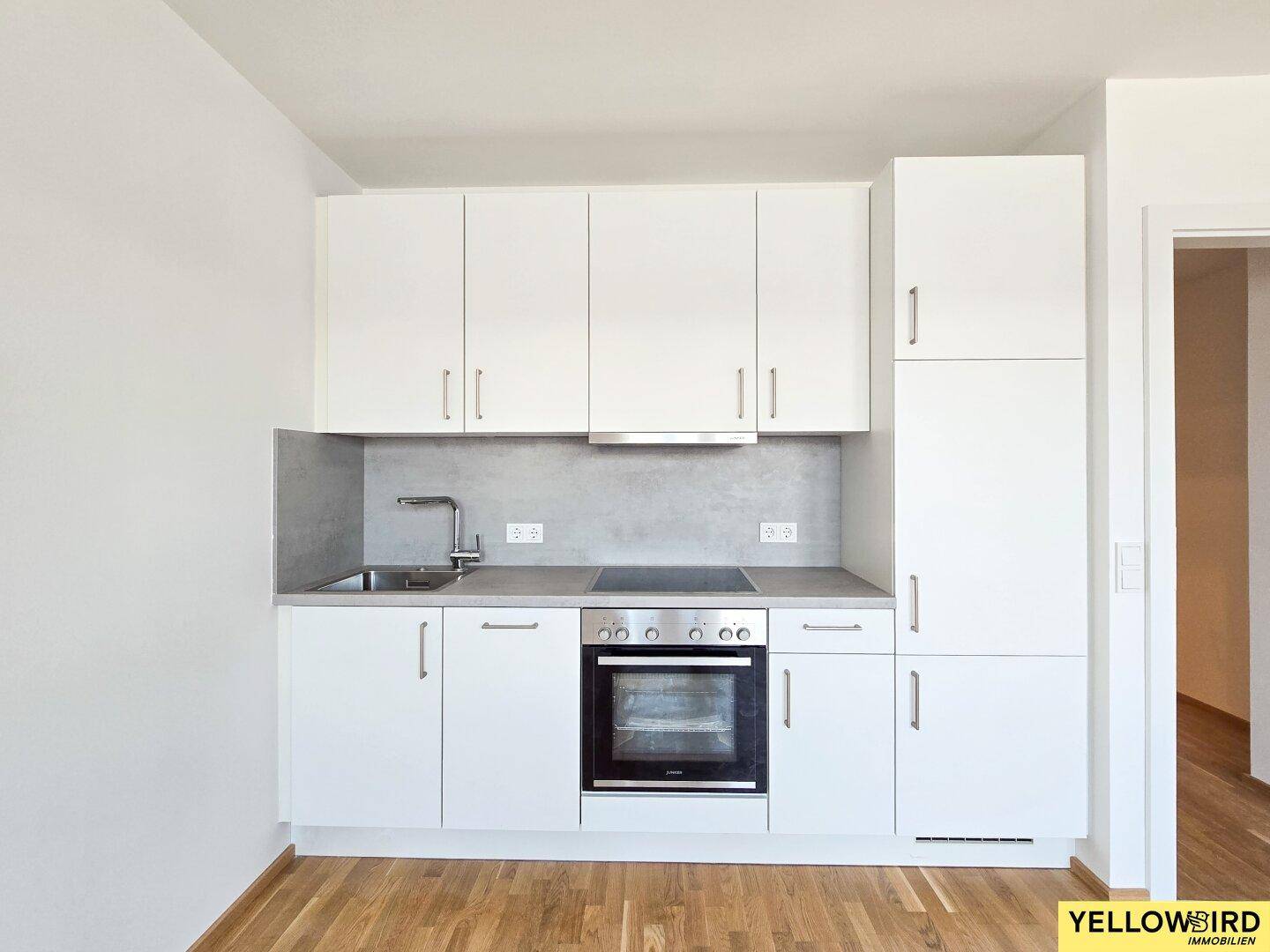 Moderne Küchenzeile mit weißen Schränken, integriertem Backofen und Kochfeld in neuwertigem Zustand.