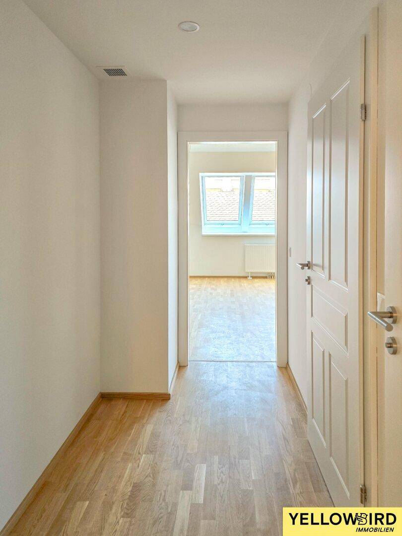 Heller Flur mit Holzboden und Zugang zu einem weiteren Zimmer mit Dachfenstern im Obergeschoss.