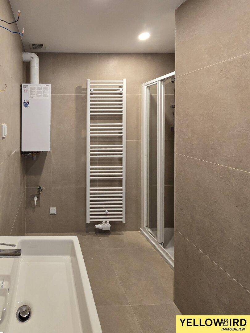 Modernes Badezimmer mit Duschkabine, Waschbecken und beheiztem Handtuchhalter, komplett gefliest.