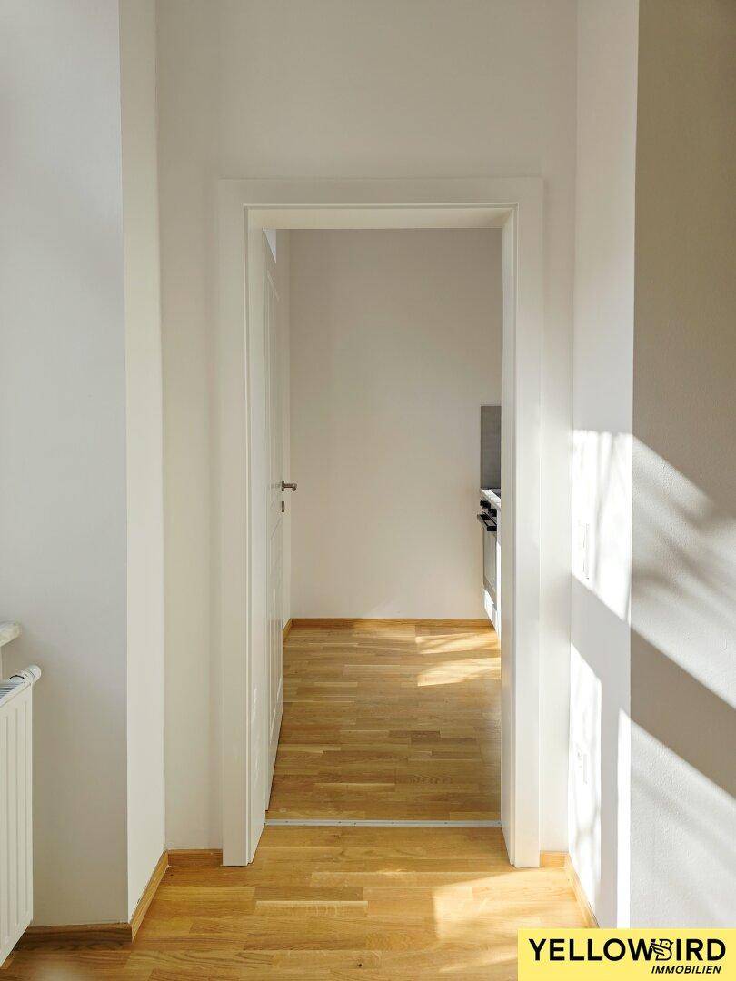 Heller Durchgang mit Holzboden, der zu einem weiteren Raum führt, beleuchtet von natürlichem Licht.