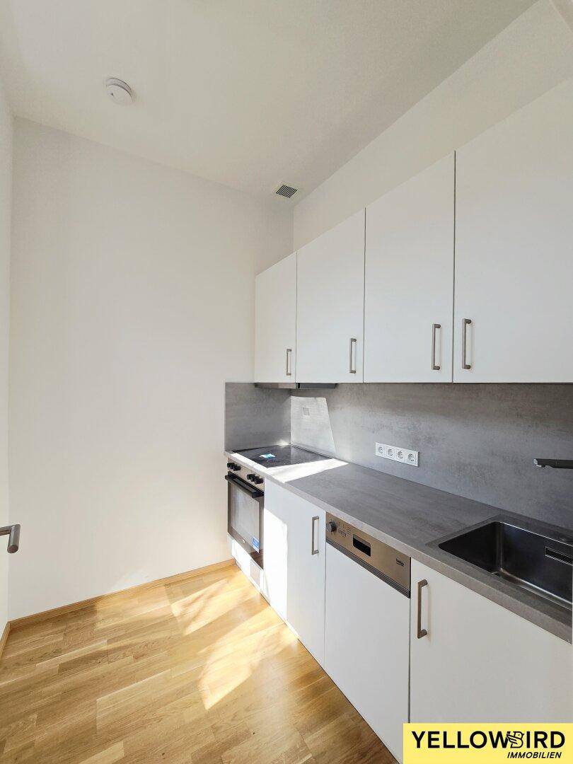 Moderne Einbauküche mit weißen Schränken, grauer Arbeitsplatte, Spüle und integrierten Geräten.