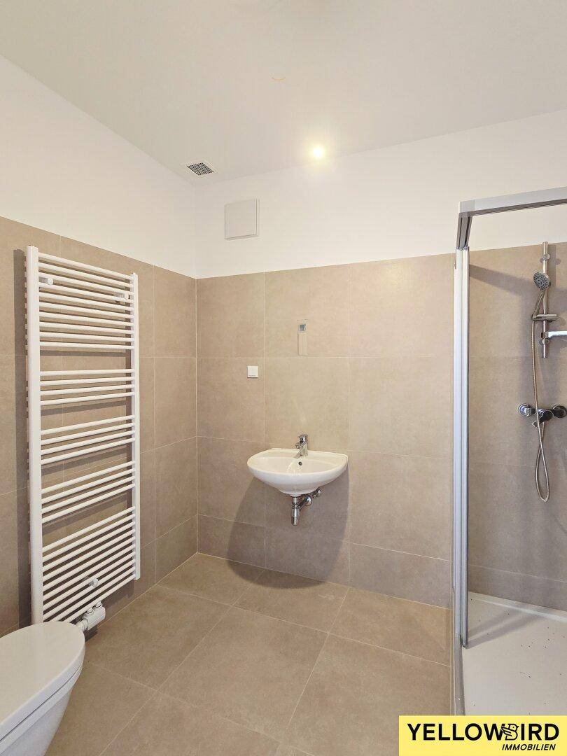 Modernes Badezimmer mit beigefarbenen Fliesen, Dusche, Waschbecken und beheiztem Handtuchhalter.