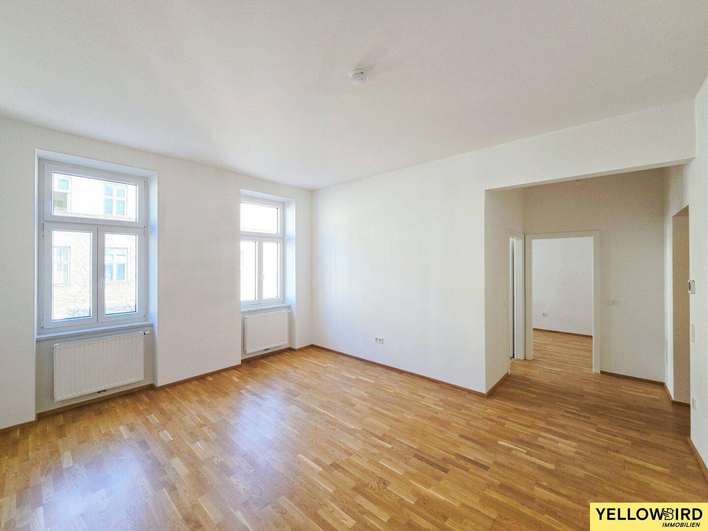 Geräumiges, unmöbliertes Wohnzimmer mit Parkettboden und großen Fenstern, bereit zur individuellen Gestaltung.