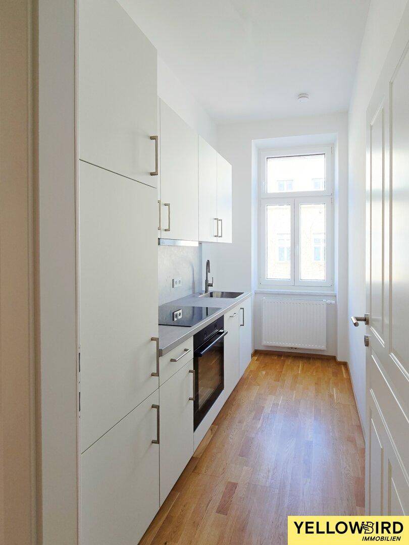 Schmale, moderne Küche mit weißen Schränken, integrierten Geräten und Fenster.