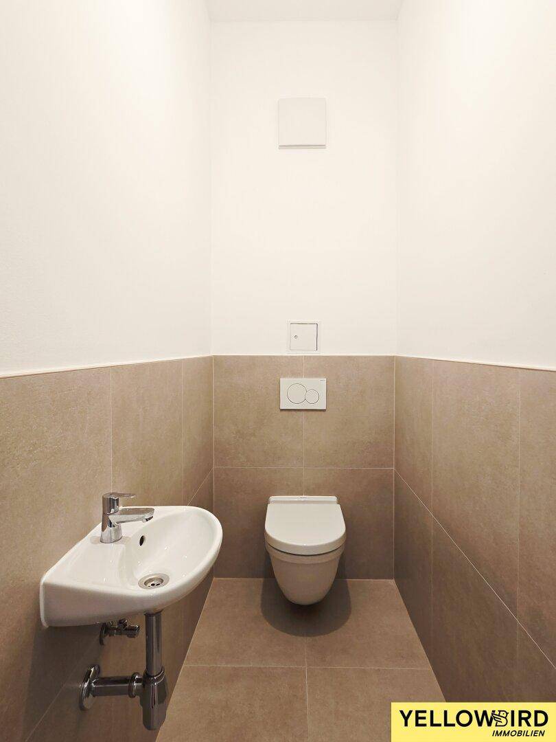 Separate Toilette mit Wand-WC und kleinem Waschbecken, modern gefliest.