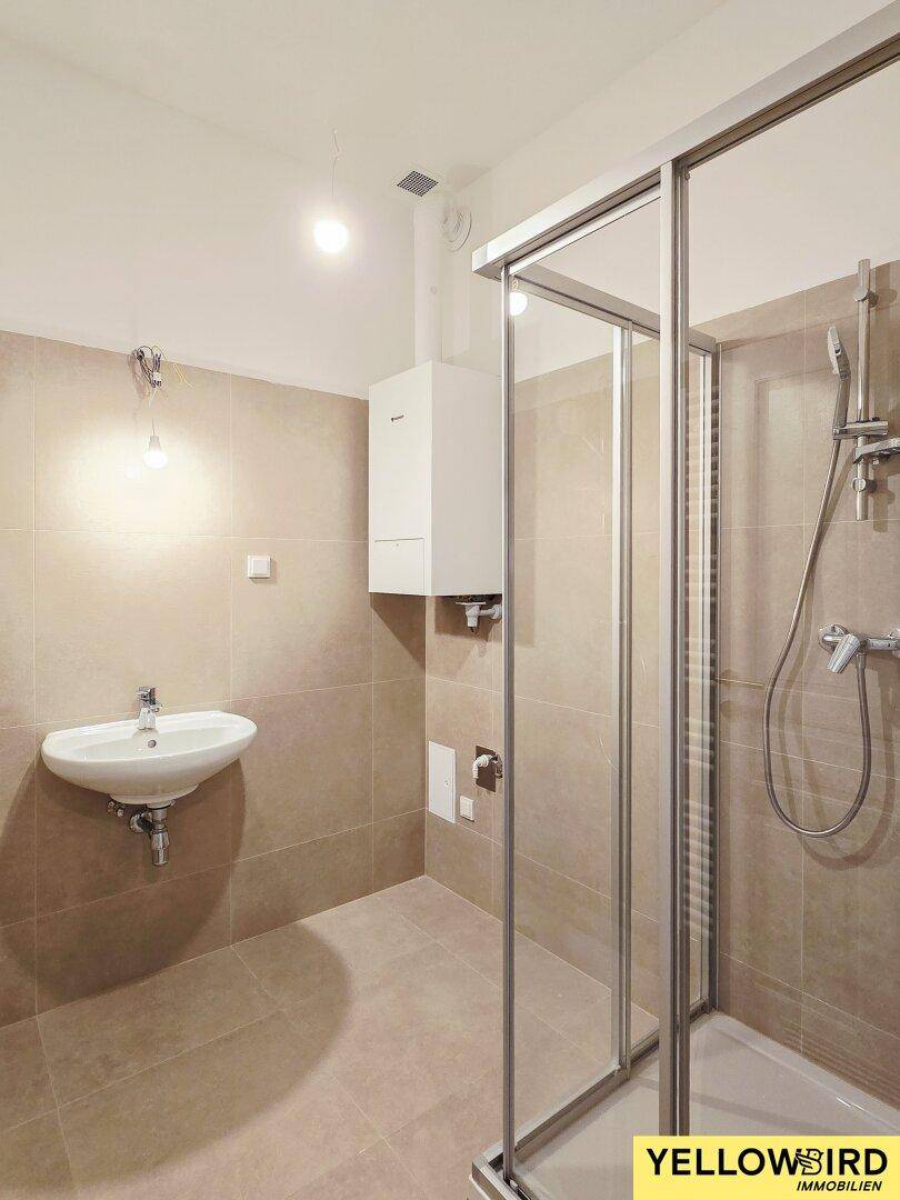 Modern gefliestes Badezimmer mit Duschkabine, Waschbecken und Gastherme.
