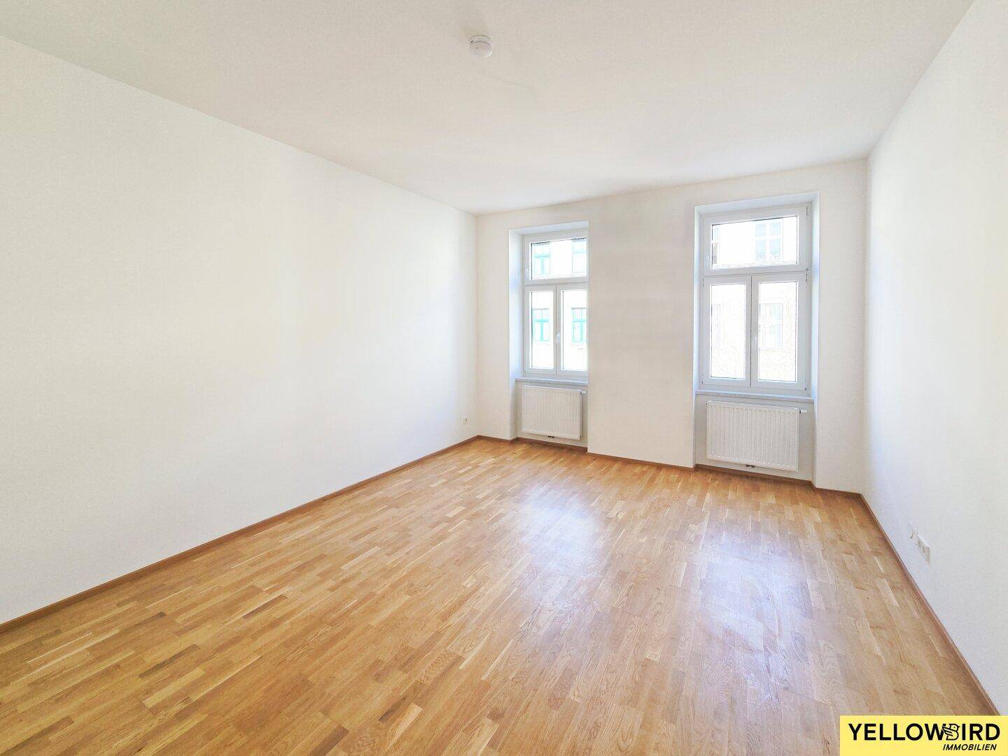 Leerer Raum mit hellem Holzboden und zwei großen Fenstern, bereit zur individuellen Gestaltung und Nutzung.