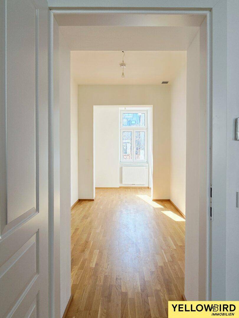 Heller Flur mit Holzboden, der zu einem weiteren Raum mit Fenster führt und viel Tageslicht bietet.