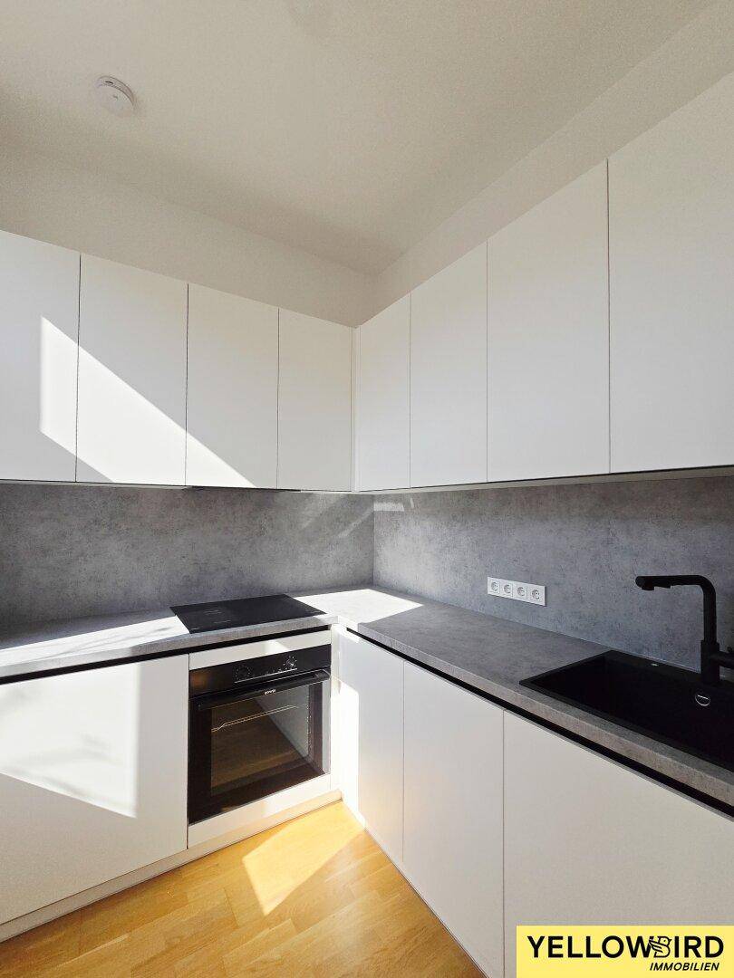 Moderne Einbauküche mit weißen Fronten, dunkler Arbeitsplatte, Spüle und integriertem Backofen.