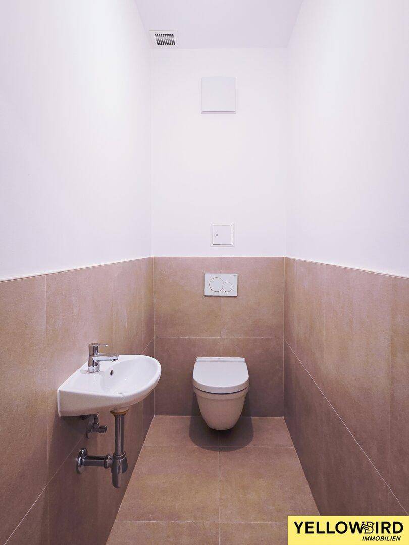 Modernes Gäste-WC mit Wand-WC, kleinem Waschbecken und beigefarbenen Fliesen.