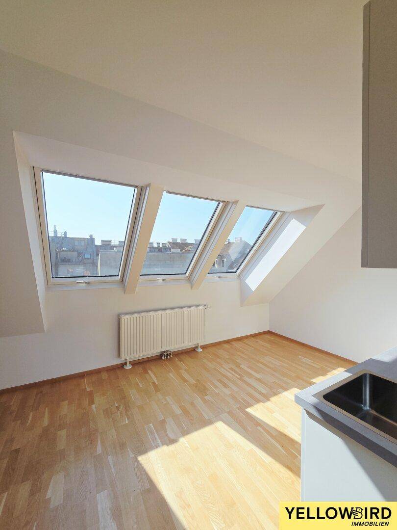 Heller Raum im Dachgeschoss mit Holzboden, Dachfenstern und Blick auf die Stadt.