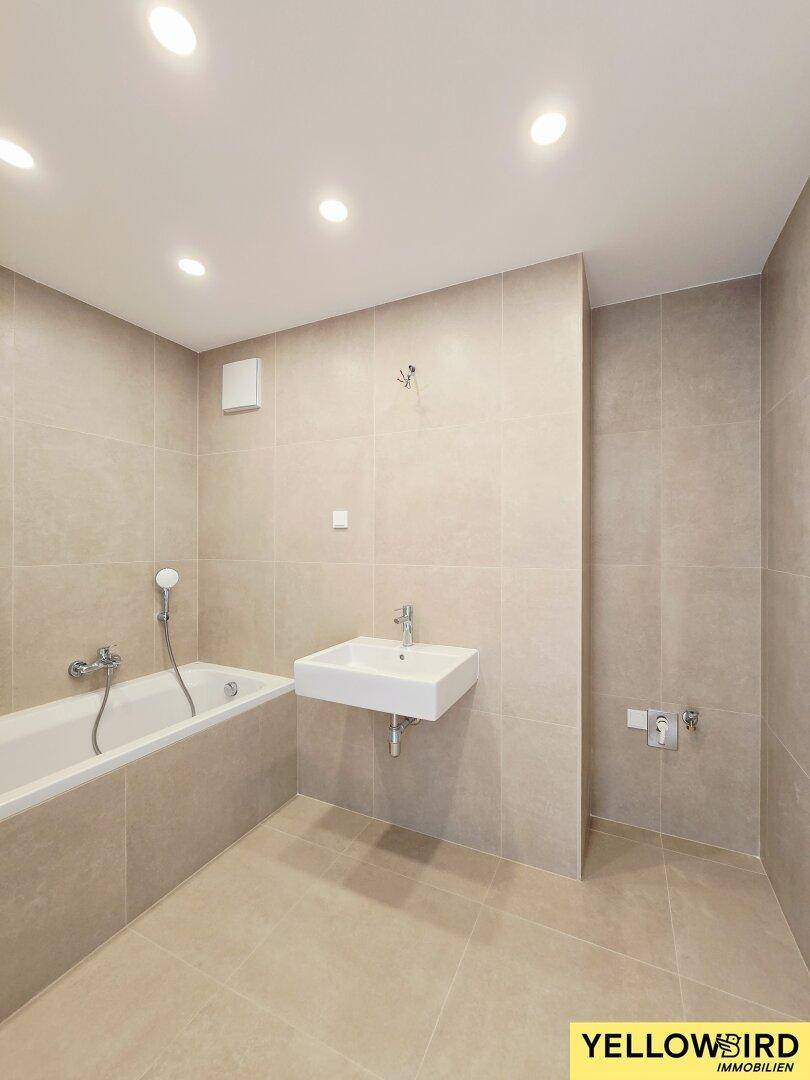 Modernes Badezimmer mit beigefarbenen Fliesen, Badewanne und Einbaustrahlern.