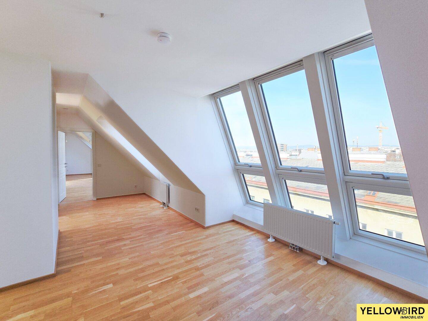 Heller Dachgeschoss-Wohnraum mit schrägen Wänden, großen Fenstern und Holzboden.