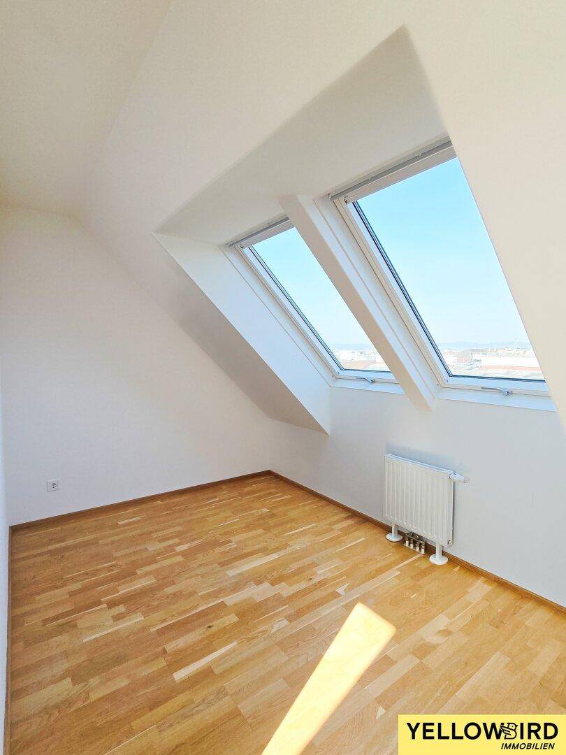 Helles Dachzimmer mit schrägen Wänden, Dachfenstern und Holzboden.