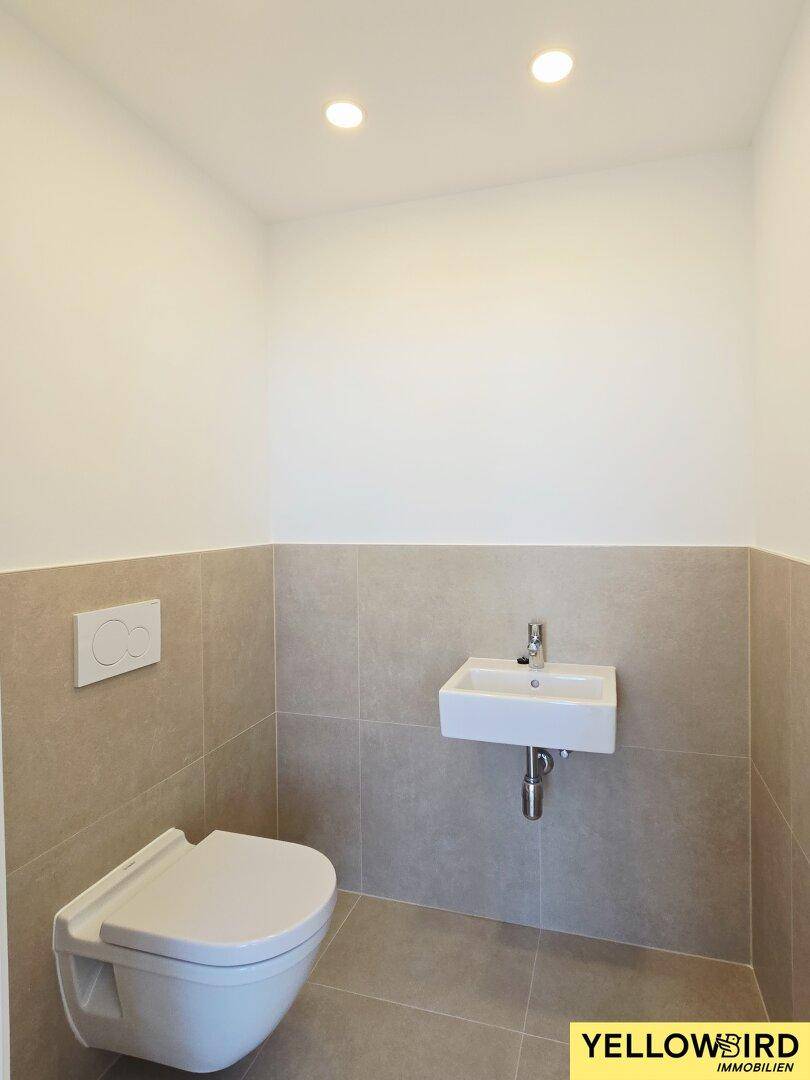 Modernes Gäste-WC mit Wand-WC, kleinem Waschbecken und Fliesenboden.