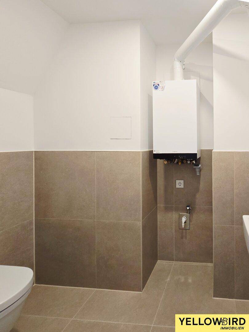 Gäste-WC mit Wand-WC, Fliesenboden und sichtbarem Warmwasserbereiter.