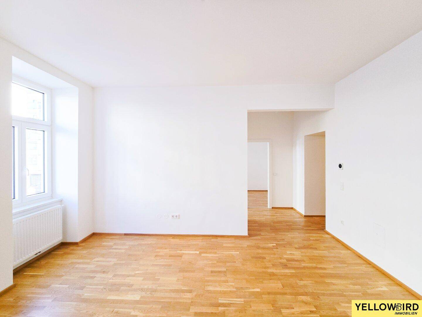 Geräumiges, leeres Wohnzimmer mit hellem Parkettboden und großen Fenstern, bereit zur individuellen Gestaltung.