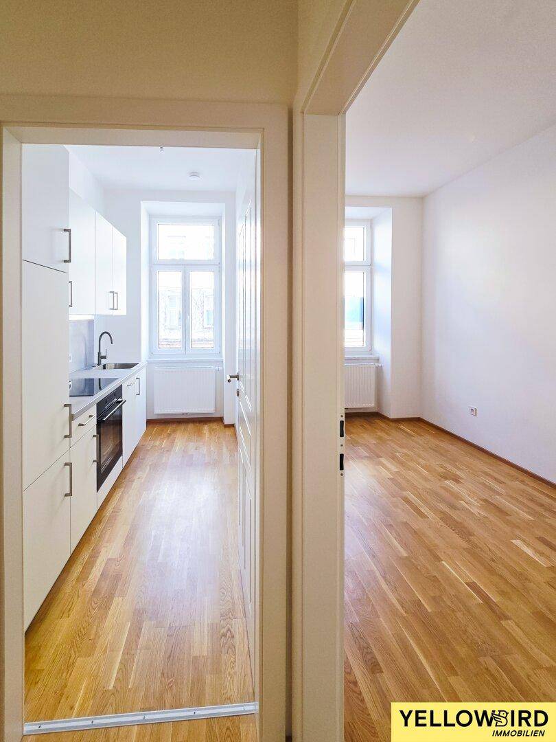 Blick durch eine Tür in eine moderne Küche und einen angrenzenden Raum mit Parkettboden.