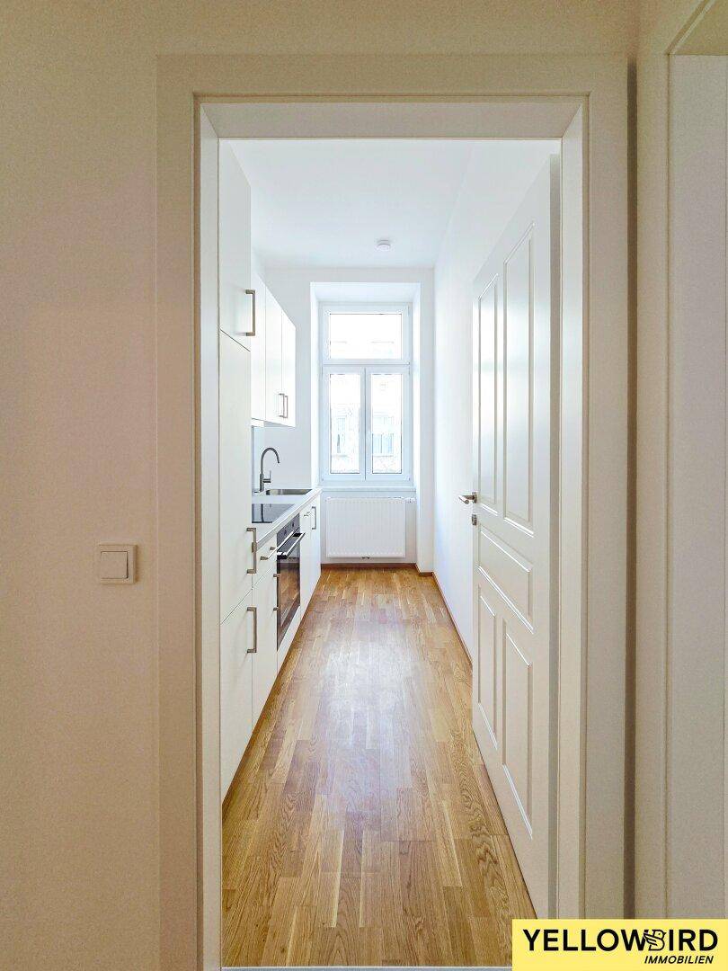Schmale, helle Küche mit modernen weißen Einbauschränken, Spüle und Fenster, effizient und funktional.