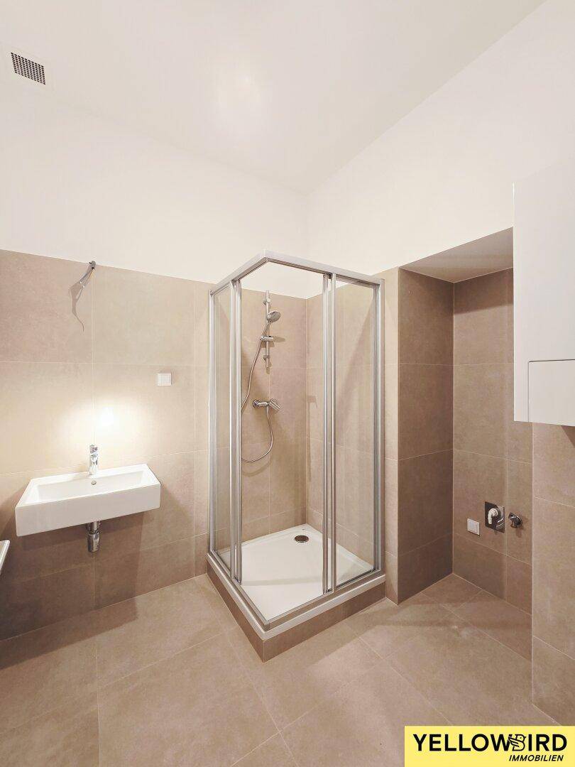 Modernes Badezimmer mit beigefarbenen Fliesen, Duschkabine und Waschbecken, funktional und sauber.