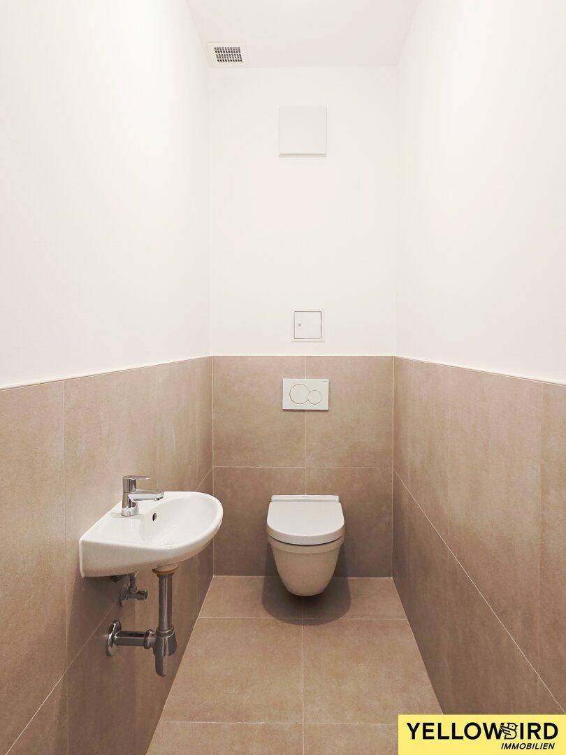 Modernes Gäste-WC mit Wand-WC, kleinem Waschbecken und beigefarbenen Fliesen.