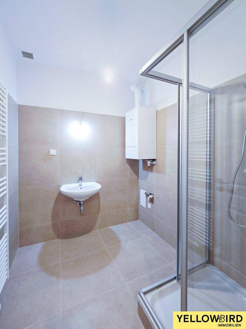 Modernes Badezimmer mit Duschkabine, Waschbecken und Heizkörper, in hellen Beigetönen gefliest.