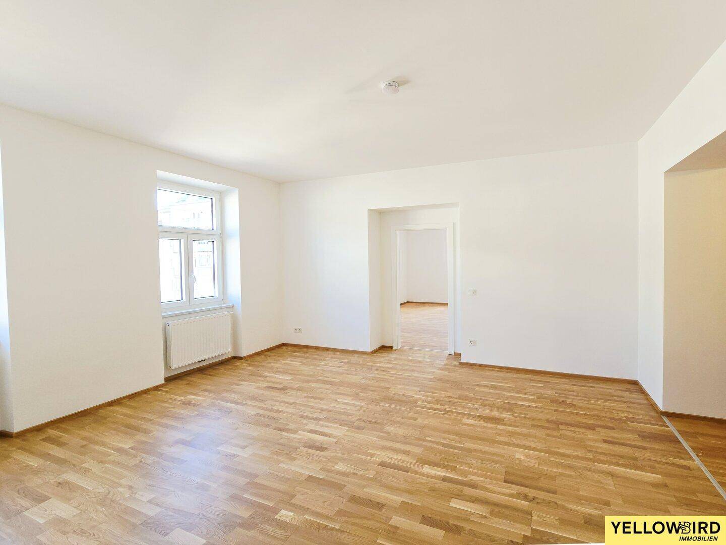 Helles Zimmer mit Parkettboden und offenem Durchgang zu einem weiteren Raum, ideal für flexible Nutzung.